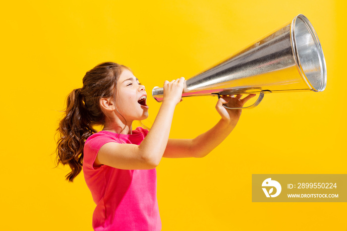 Emotional little girl, kid in casual style clothes shouting at retro speaker isolated over bright yellow background. Concept of emotions, fashion, beauty, school and ad, news