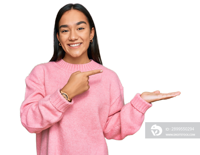 Young asian woman wearing casual winter sweater amazed and smiling to the camera while presenting with hand and pointing with finger.