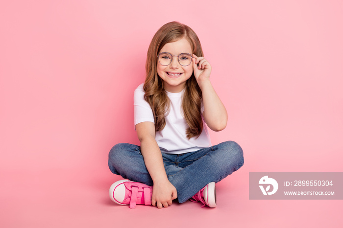 Photo of dream funny little girl sit floor wear glasses white t-shirt jeans shoes isolated pink color background