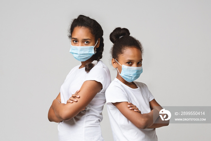 Two young sisters wearing medical masks, staying back to back