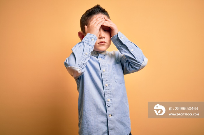 Young little boy kid wearing elegant shirt standing over yellow isolated background with hand on head for pain in head because stress. Suffering migraine.