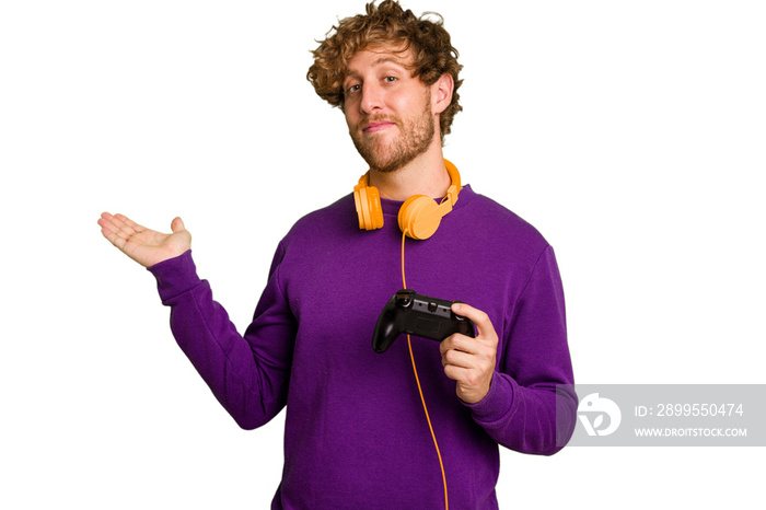 Young caucasian gamer man holding a game controller isolated on white background showing a copy space on a palm and holding another hand on waist.