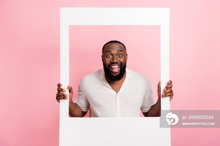 Portrait of positive guy open mouth look through paper album card isolated on pink color background