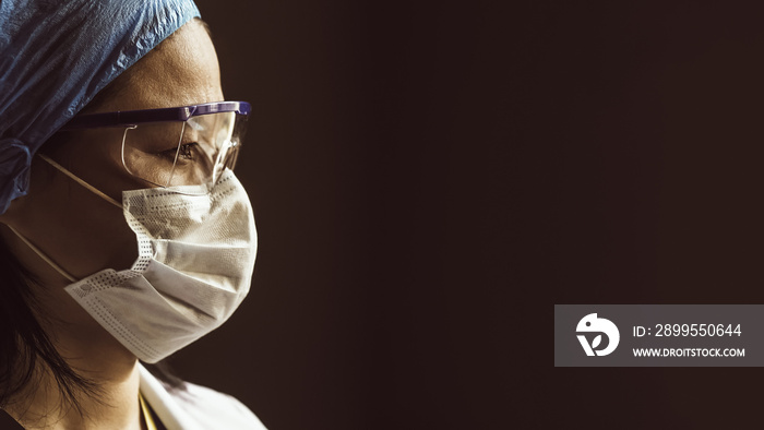 Woman in mask and goggles isolated on gray background. Profile view of female lab assistant looking at right side with copy space. Close up shot. Toned image.