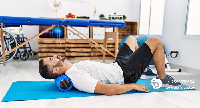 Young hispanic man patient smiling confident having neck rehab session using foam roller at clinic