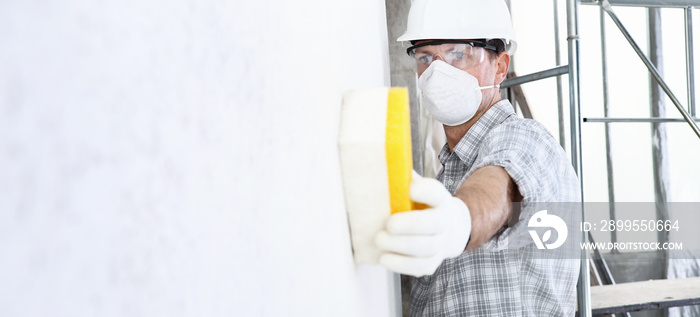 man builder using a sponge on wall professional construction worker with mask, safety hard hat, gloves and protective glasses. interior building site, copy space background