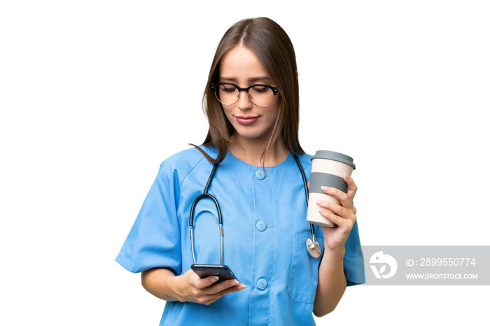 Young nurse caucasian woman over isolated background holding coffee to take away and a mobile