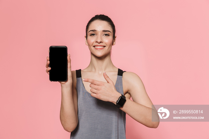 Amazing beautiful young pretty fitness woman showing display of mobile phone isolated over pink wall background.