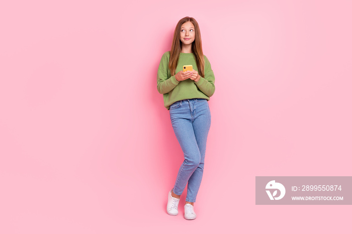 Full length photo of sweet dreamy schoolgirl wear green sweatshirt chatting modern gadget looking empty space isolated pink color background