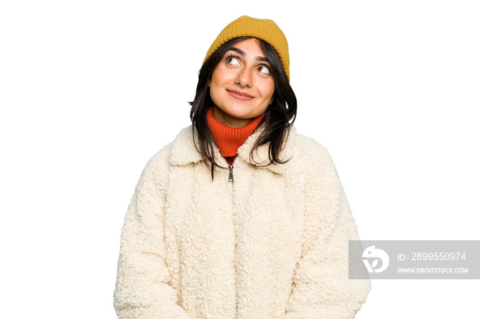 Young Indian woman wearing winter jacket and a wool cap isolated dreaming of achieving goals and purposes