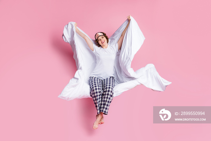 Full size photo of cheerful lady morning sit bed hold warm blanket under head stretching wake up wear mask white t-shirt plaid pajama pants barefoot isolated pink color background