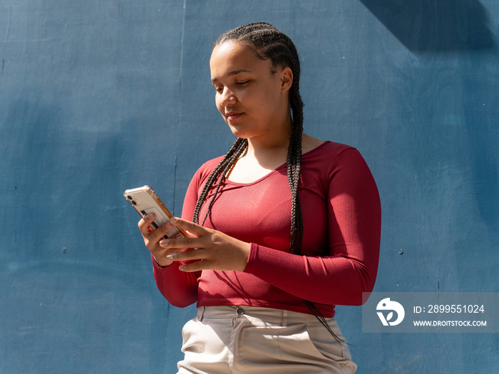 Young woman using smart phone against blue wall