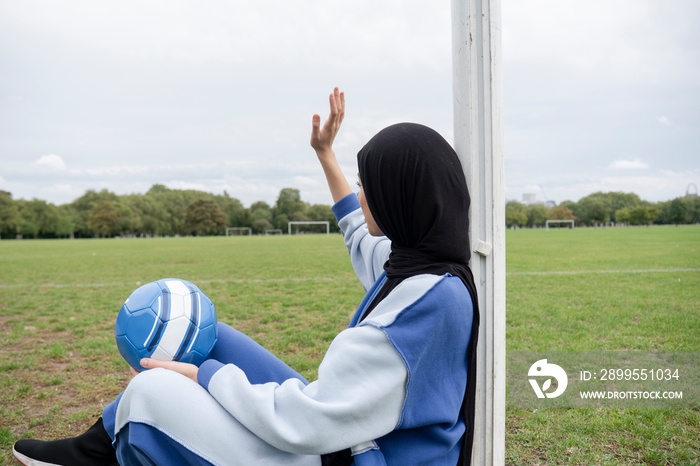 Woman in hijab sitting in soccer field with soccer ball