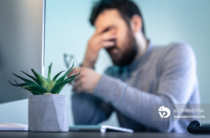 A tired man rubs his eyes in front of a computer screen.