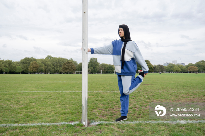 Woman in hijab stretching leg in soccer field