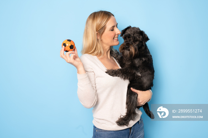 Cute young woman hugs her puppy schnauzer dog. Love between owner and dog. Isolated on blue background. Studio portrait.