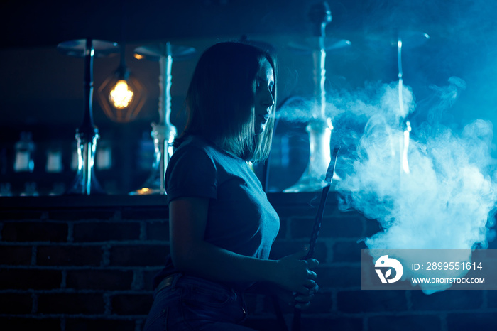 Beautiful woman in night club smoke hookah or shisha bar, blue background