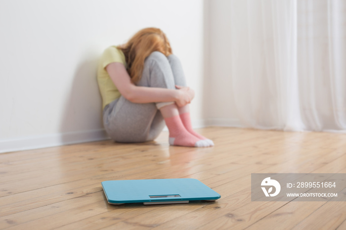 sad teenager girl with scale on wooden floor