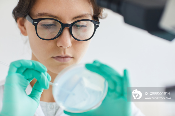 Close up portrait of beautiful young woman holding petri dish while working on research in medical laboratory, copy space