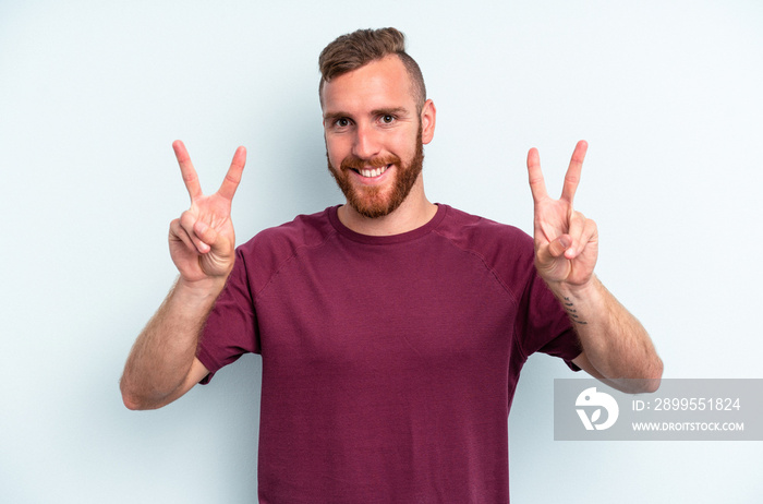 Young caucasian man isolated on blue background showing victory sign and smiling broadly.