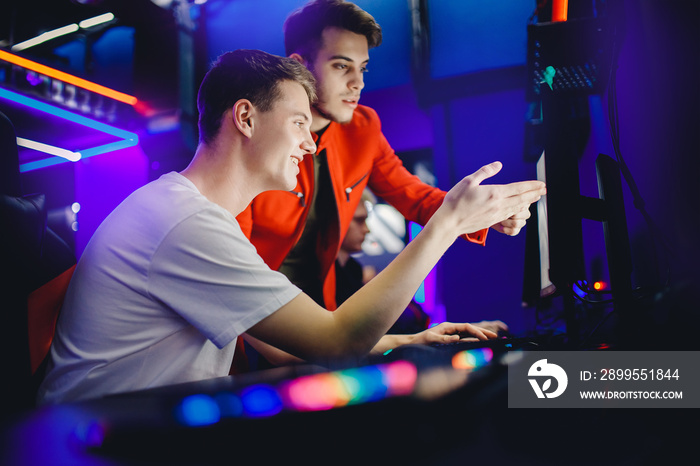 Team of two guys playing online video games analyzes strategy of fighting behind computer monitor in Internet cafe