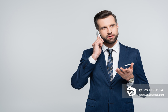 economist in blue suit pointing with hand while talking on smartphone isolated on grey.