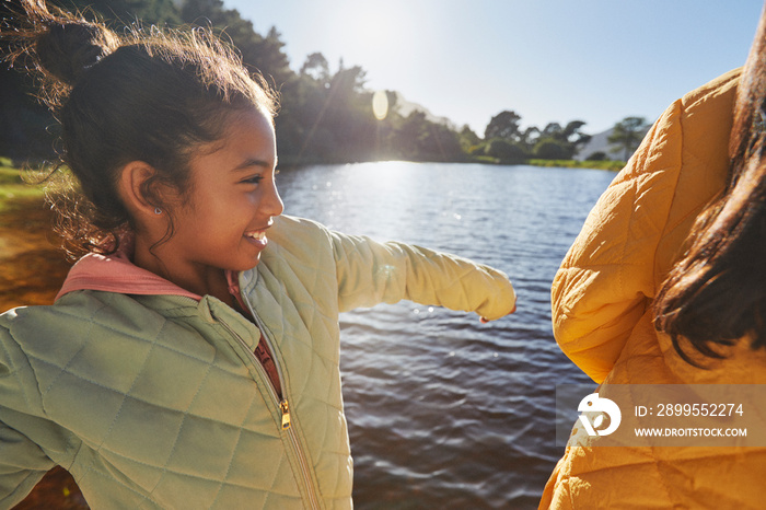 Little girl smiling and playing at lake during family camping vacation with glistening water and natural landscape