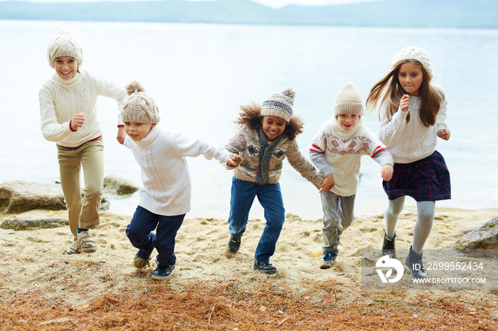 Group of happy children playing outdoors running on lake shore on warm autumn day all dressed in similar knit clothes