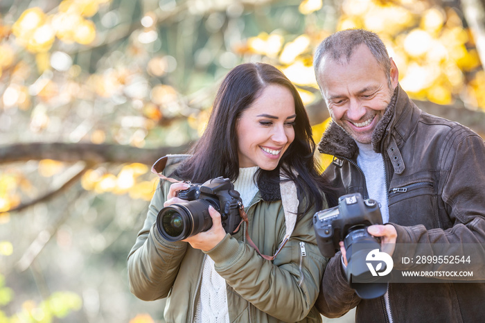 Professional photographer teaches photography to his student outdoors, both smiling at the picture in his camera