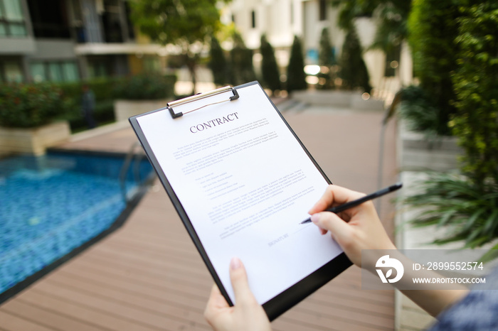 large hand portrait of subscribers sign contract on background of new building with swimming pool. concept of long-term rental housing or short-term apartment rental travel. Front used with Open Font