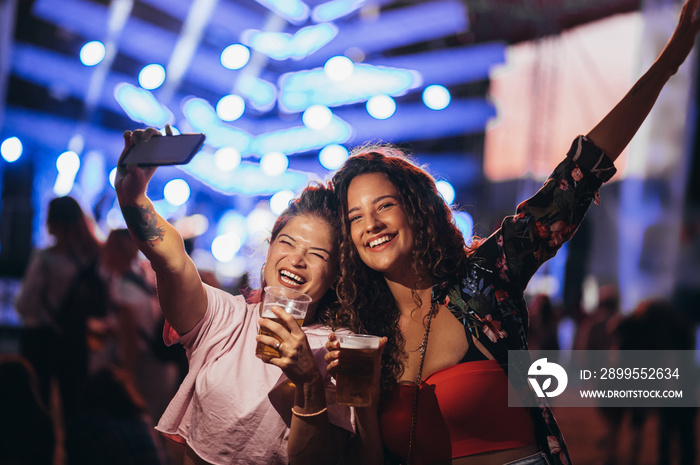 Two beautiful friends taking selfie with a samrtphone on a music festival