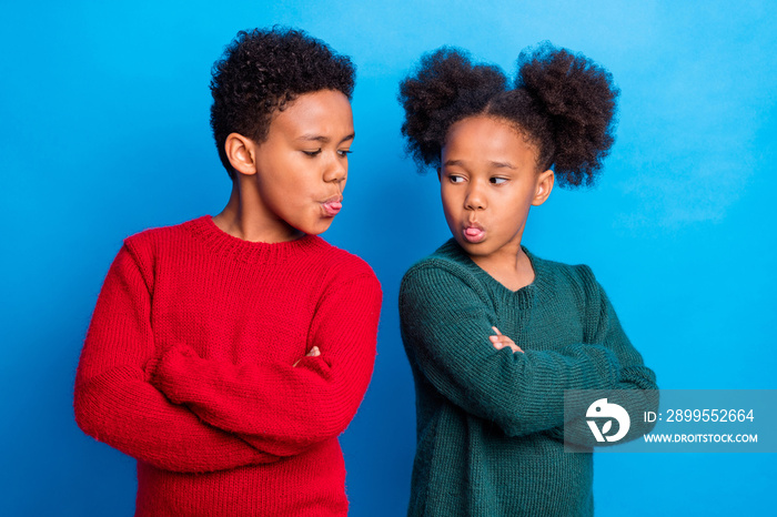 Photo of moody angry dark skin children wear pullovers arms crossed showing tongues isolated blue color background