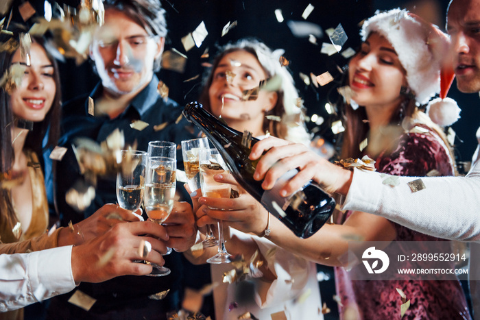 Pouring champagne. Group of cheerful friends celebrating new year indoors with drinks in hands