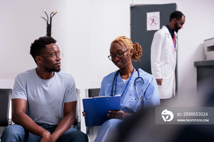 Health specialist examining young man in waiting area lobby, taking notes on report papers to give medication with insurance support. Patient and nurse doing checkup consultation in waiting room.