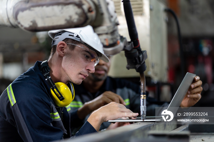 Male engineer worker working with computer notebook for control automatic robotic arm machine in the factory. Male technician worker maintenance automatic robotic hand in smart factory