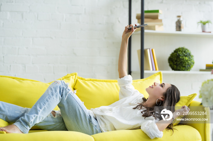 a beautiful young woman lounging on a sofa, is using an application in her smart phone device