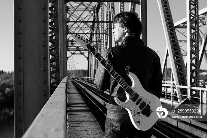 Monochrome man with an electric guitar in the industrial landscape outdoors