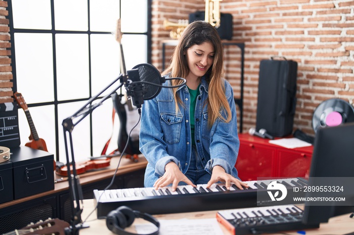 Young hispanic woman musician playing piano keyboard at music studio