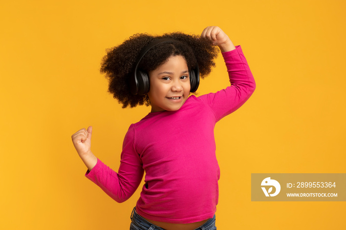 Positive funny african american girl wearing wireless headphones and dancing