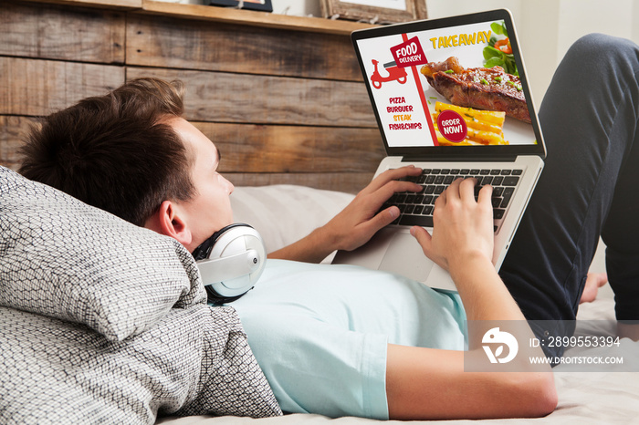 Man ordering take away food by internet with a laptop while lying at home.