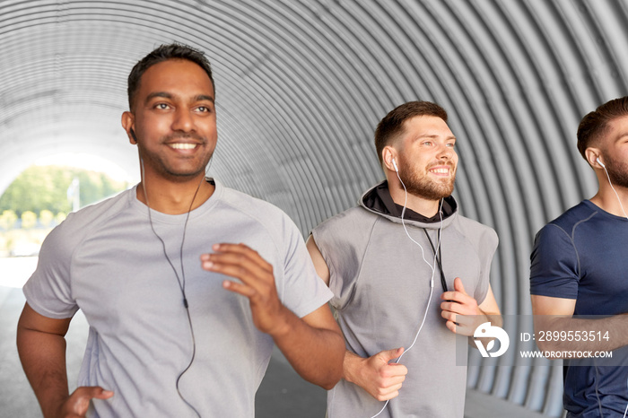 fitness, sport and healthy lifestyle concept - smiling young men or male friends with earphones running outdoors