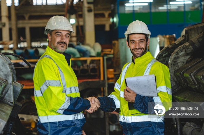 Caucasian factory engineer talking and shaking hands on business cooperation agreement. Successful hand shaking after good deal, workers handshaking each other at heavy industrial production line.