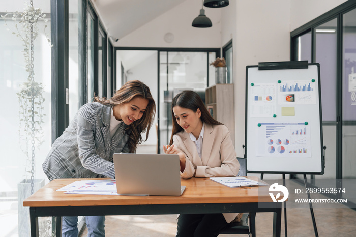 Two young pretty asia business woman in suit talking together in modern office workplace, Thai woman, southeast asian, looking on laptop together