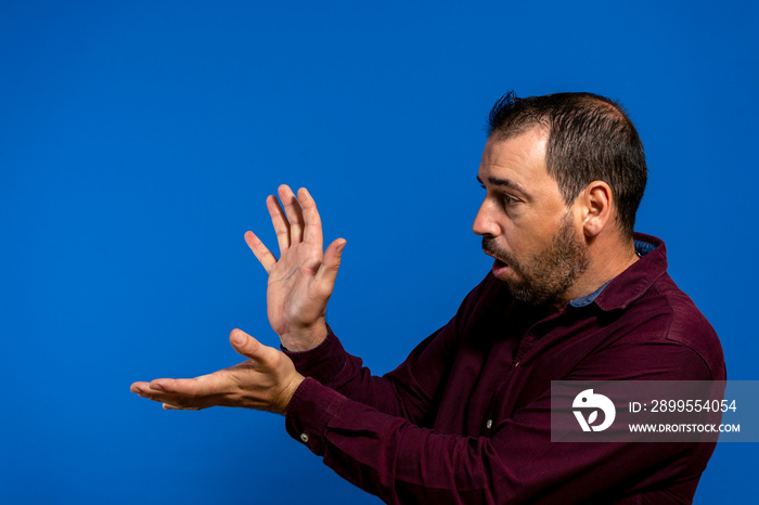 Latin bearded man dressed in a purple shirt isolated on blue studio background, he is throwing a kame hame imitating Son Goku from Dragon Ball, one of his youth heroes