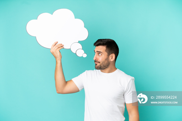 Young handsome caucasian man isolated on blue background holding a thinking speech bubble