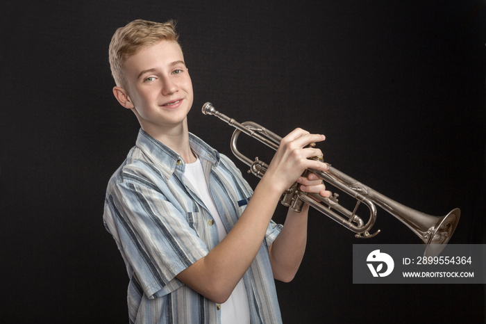 The young Boy plays jazz on a trumpet in front of dark background