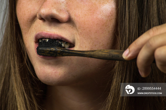 young woman brushing her teeth with a black tooth paste with active charcoal, and black tooth brush on white background for Teeth whitening