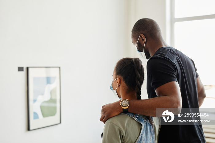 Minimal side view at African-American family looking at paintings in modern art gallery amd wearing masks, copy space