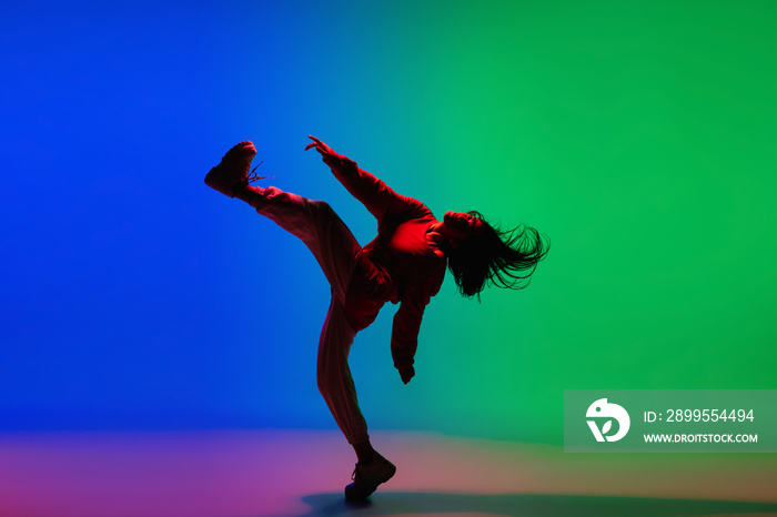 Street. Stylish sportive girl dancing hip-hop in stylish clothes on colorful background at dance hall in neon light. Youth culture, movement, style and fashion, action. Fashionable bright portrait.