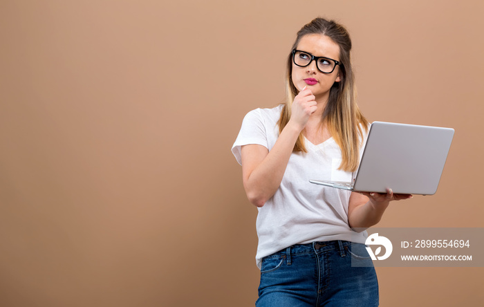 Young woman with a laptop computer in a thoughtful pose on a brown background